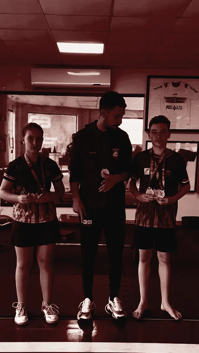 Dupla de atletas de badminton treinada pela GB, com as medalhas no peito, ao lado de Gabriel na clínica
